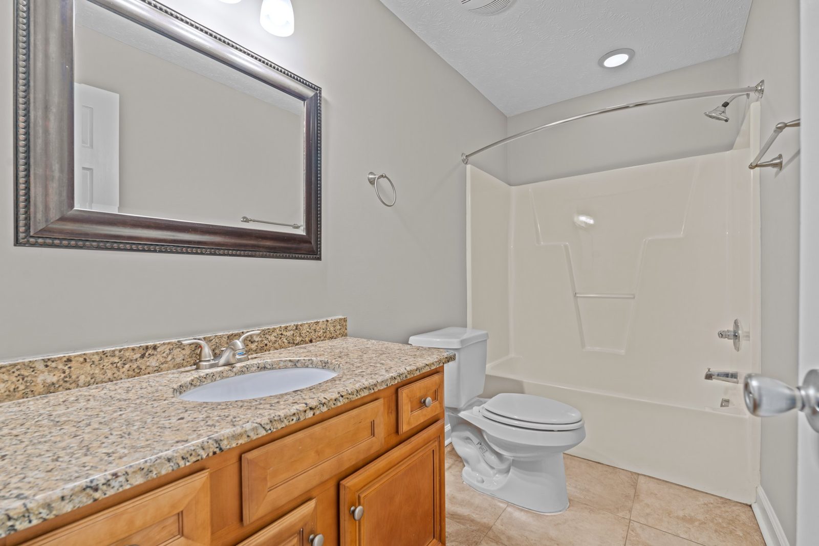 Renovated hall bathroom with a granite vanity, framed mirror and tub with shower