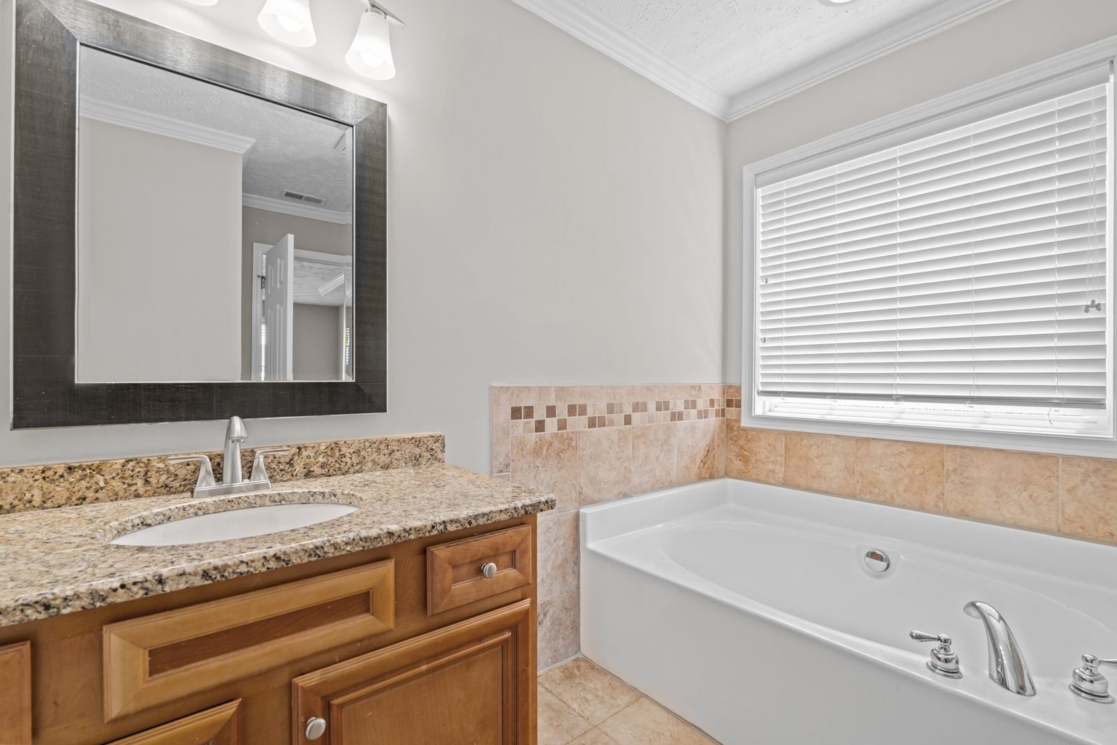 Primary bathroom with a long granite vanity and a soaking tub under a window