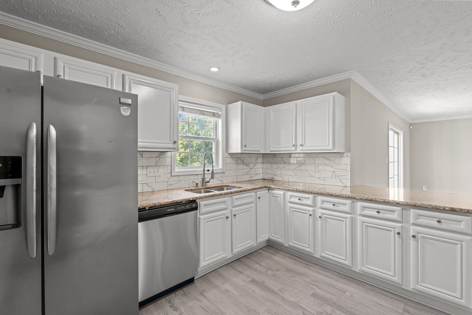 Renovated kitchen with white cabinets, stainless refrigerator and plank flooring