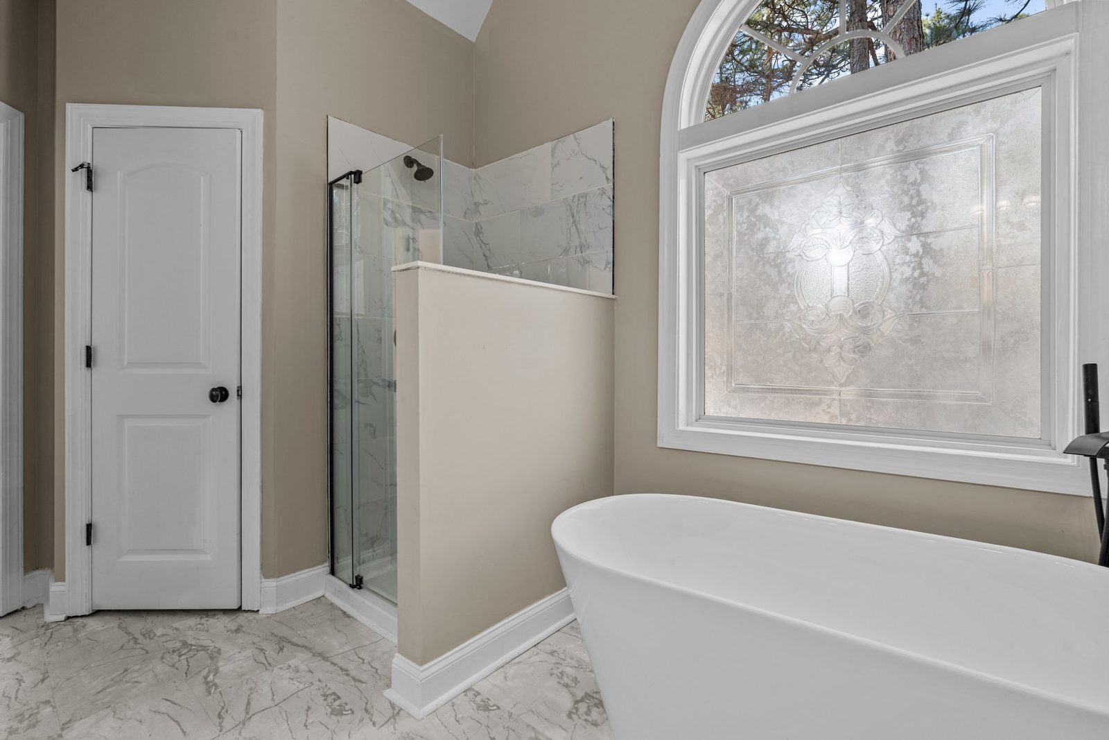 Primary bathroom with a freestanding soaking tub and arched window