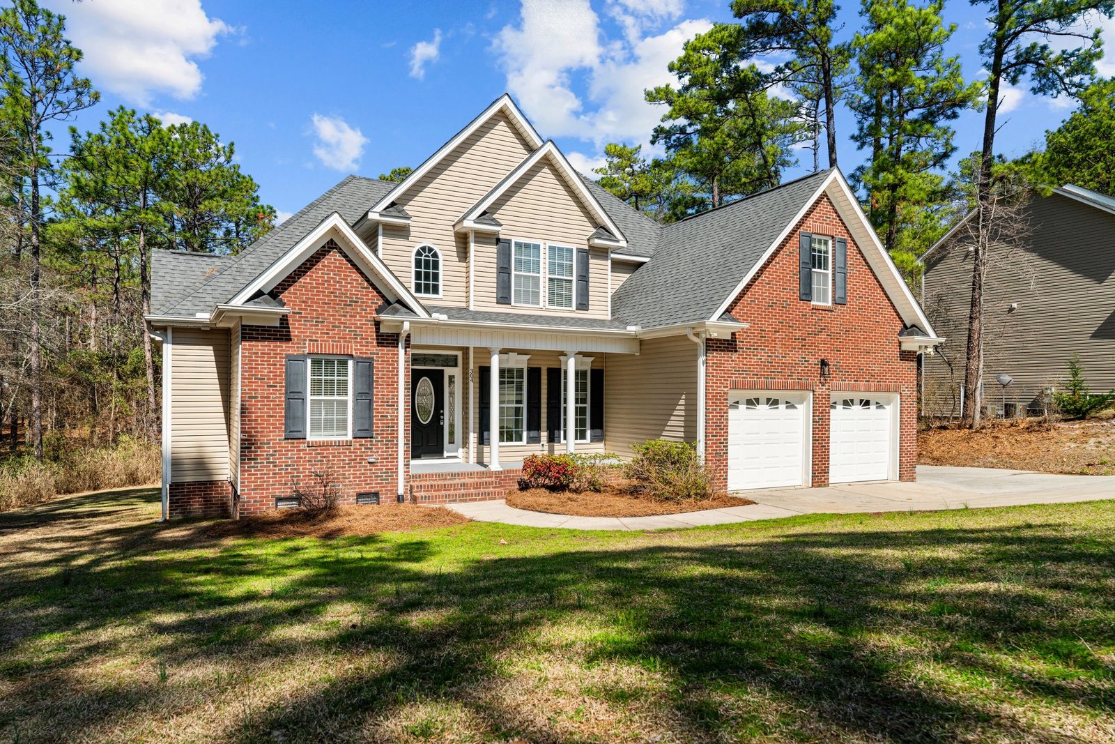 Brick home with a new gray shingle roof, front porch and pine trees