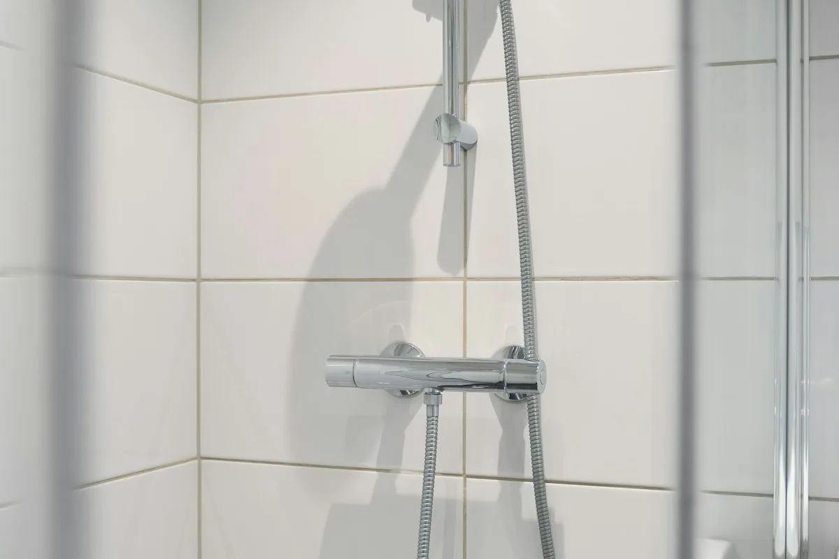 White tiled shower with a glass door and wall-mounted controls