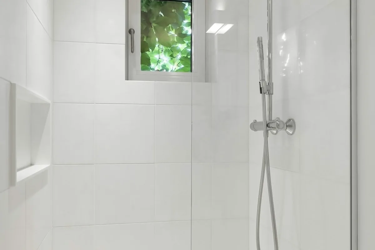 Walk-in shower with white tile next to a window