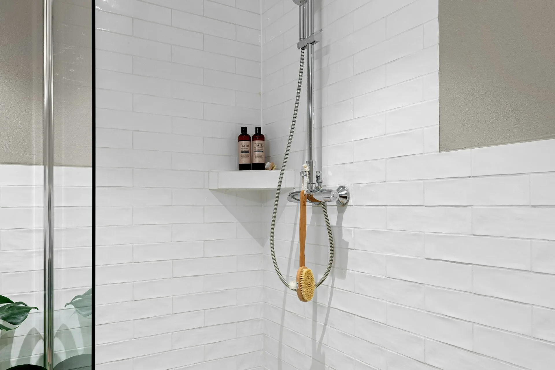 White tiled shower with a glass door and a corner shelf