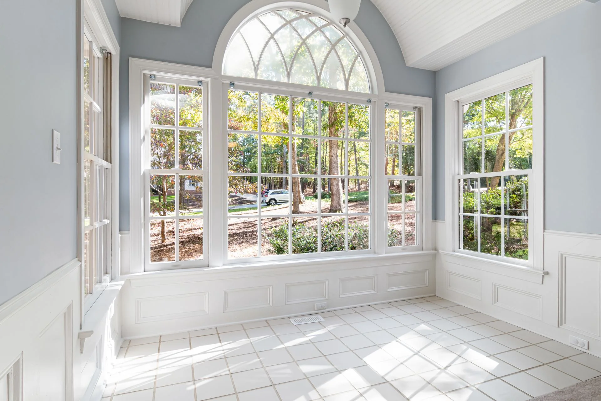 Bright sunroom with an arched window, white wainscoting and a tile floor