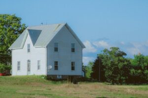 Two-story white farmhouse with a light gray metal roof under a clear blue sky